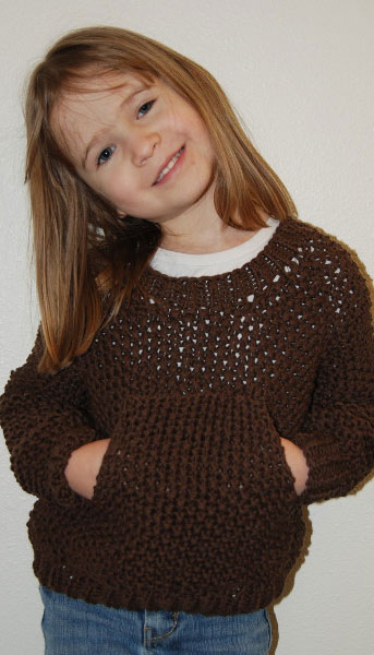 A little girl wears a dark brown handknit pullover with a kangaroo pocket in the front