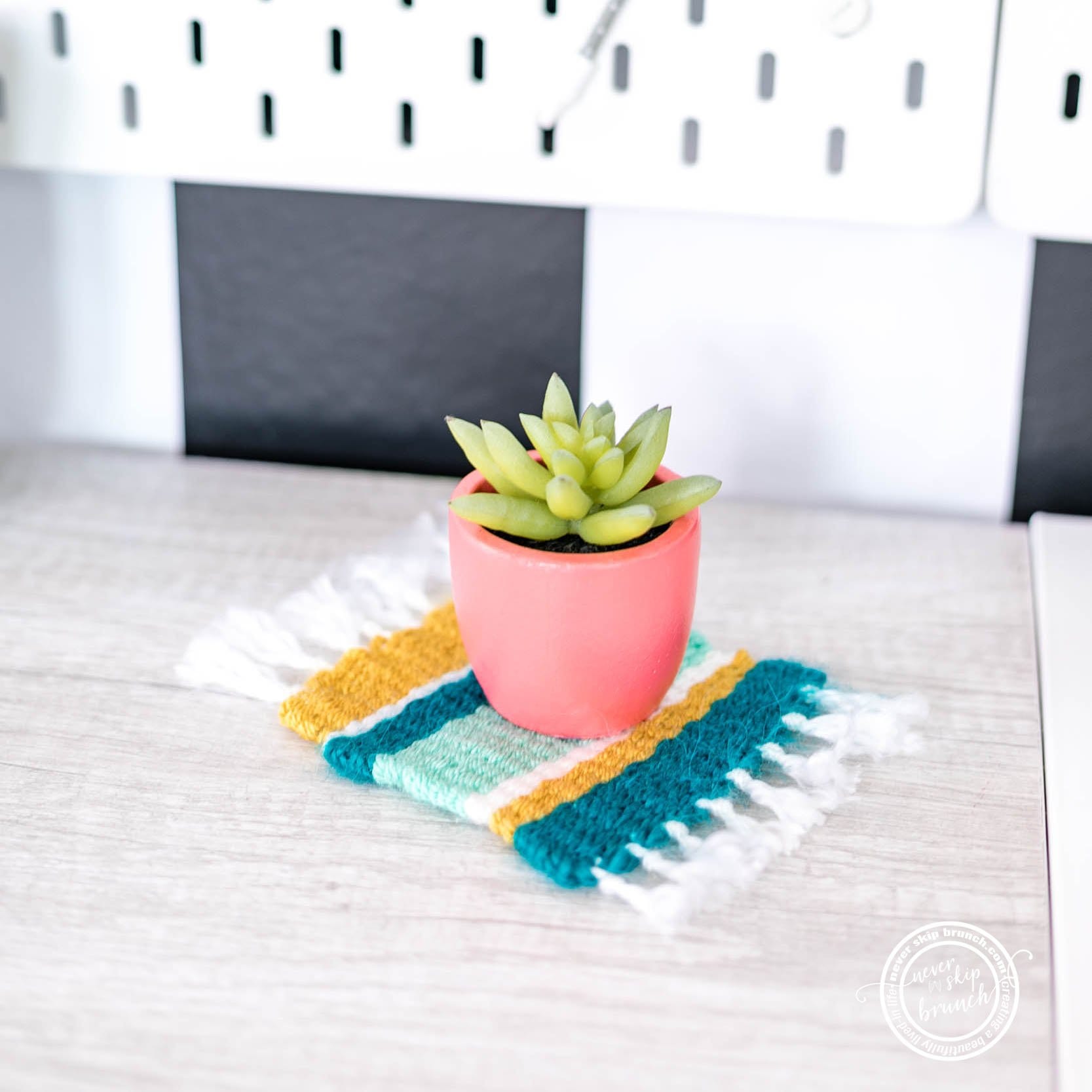 a small potted cactus sits atop a woven mug rug striped in white, turquoise, sage green and gold