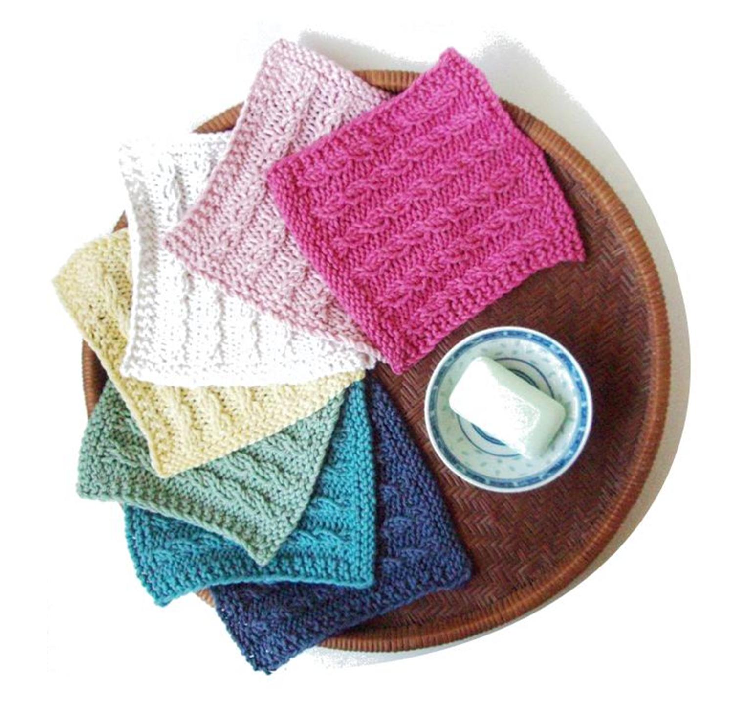 an array of colorful, handknit cabled washcloths on a wooden plate with a bar of soap