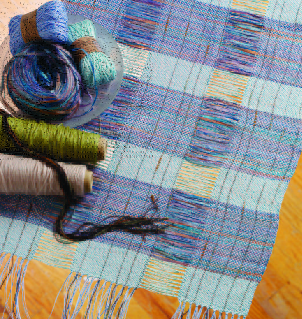 a woven table runner in shades of light blue, dark blue, purple and green, with an openwork striping effect