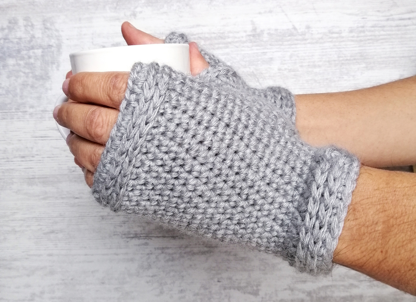 Close up on a hand clad in a light grey hand crocheted fingerless mitt