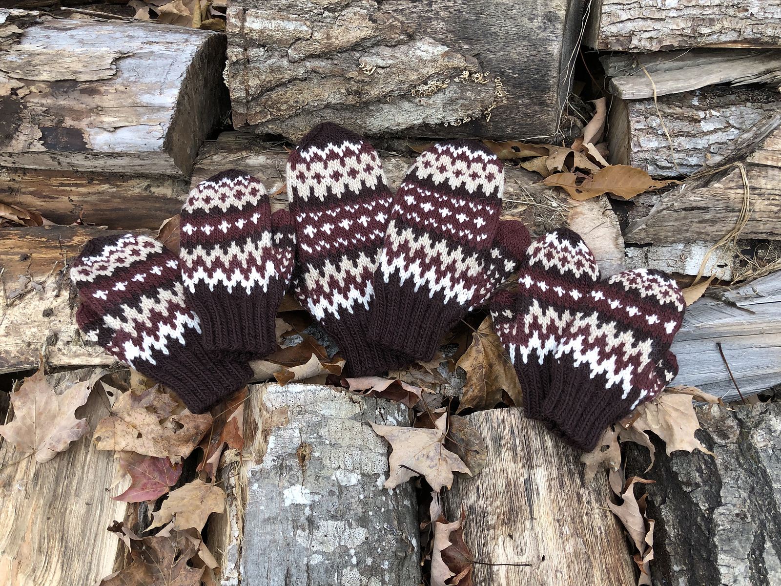 several colorwork mittens in red, brown and white lie on a pile of wood