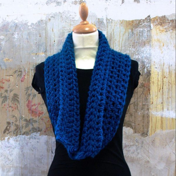 A deep blue crocheted infinity cowl hangs on a mannequin