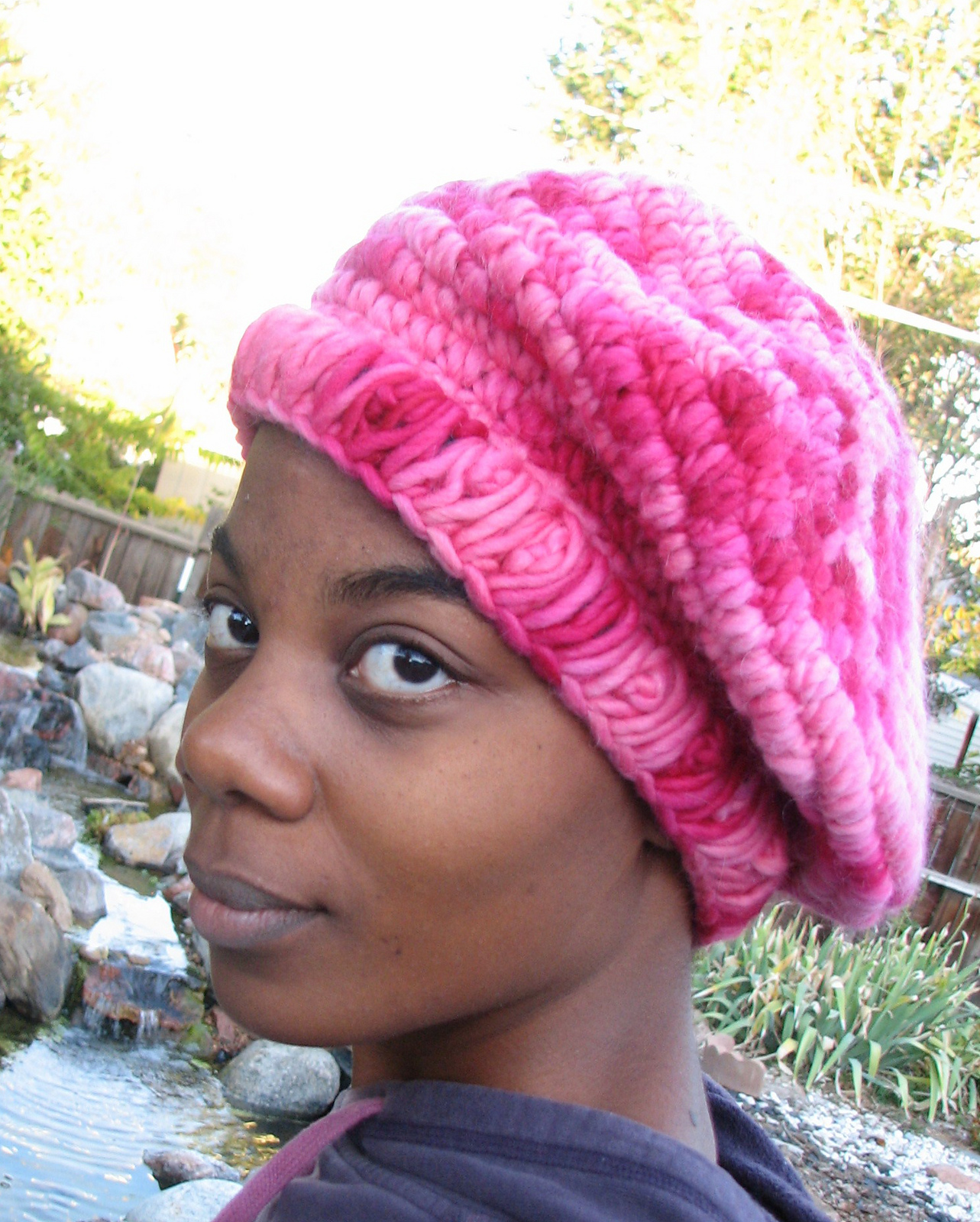 A black woman wears a beret crocheted with bright pink yarn
