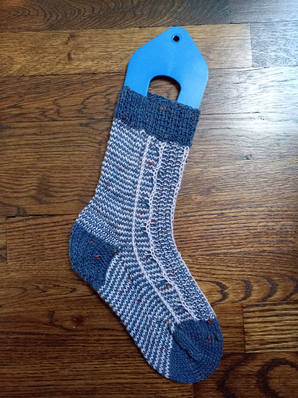  A single sock knit with blue and white yarn in a textured striped and slipped stitch pattern lies on the floor