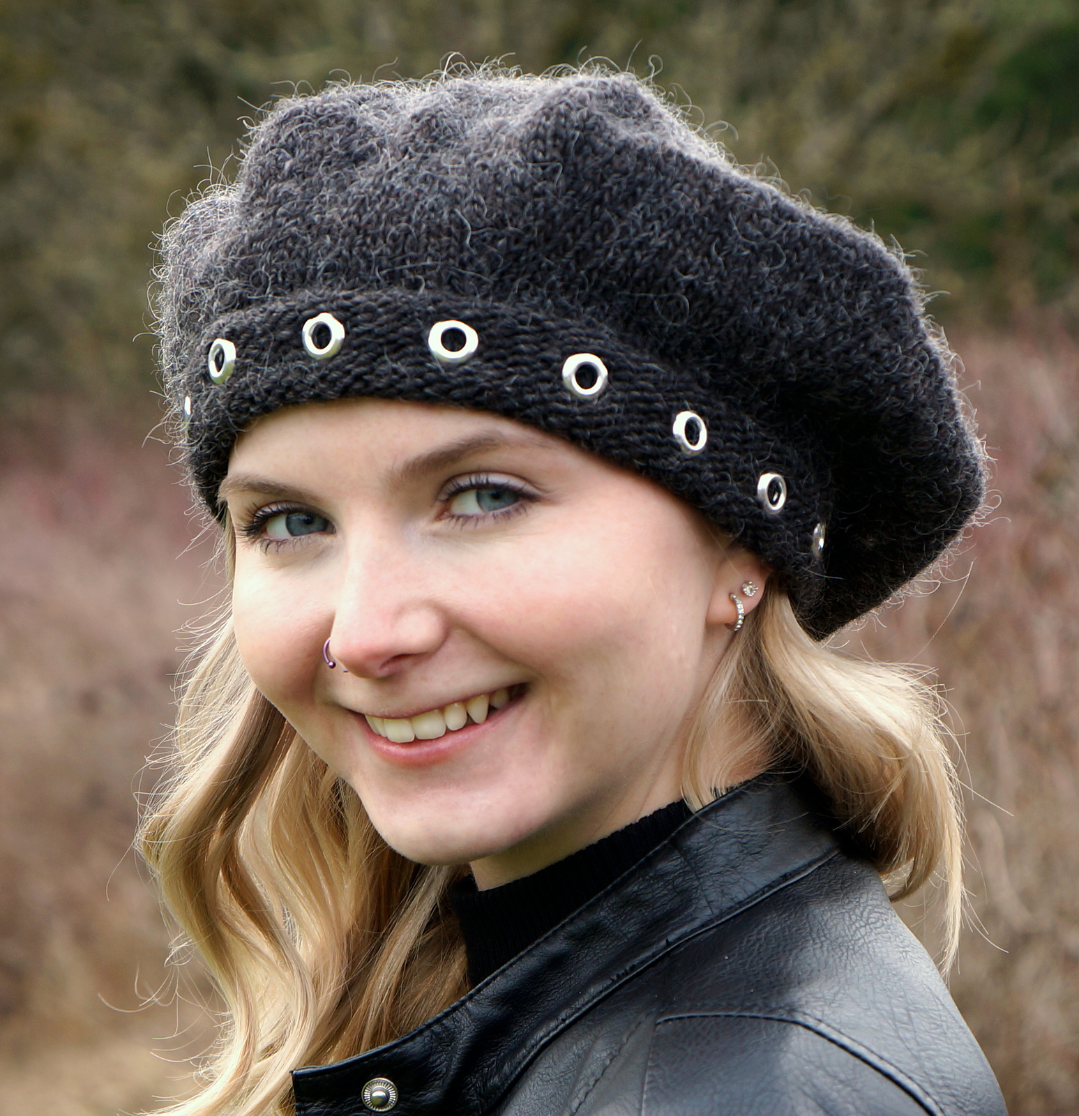close up of a white woman wearing a black knit beret with silver metal grommets adorning the brim