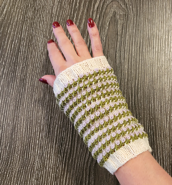 A single mitt knit in a two-color textural pattern worn by a woman's hand