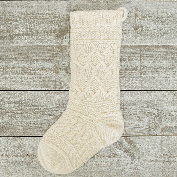 An all white handknit holiday stocking featuring a melange of cable motifs