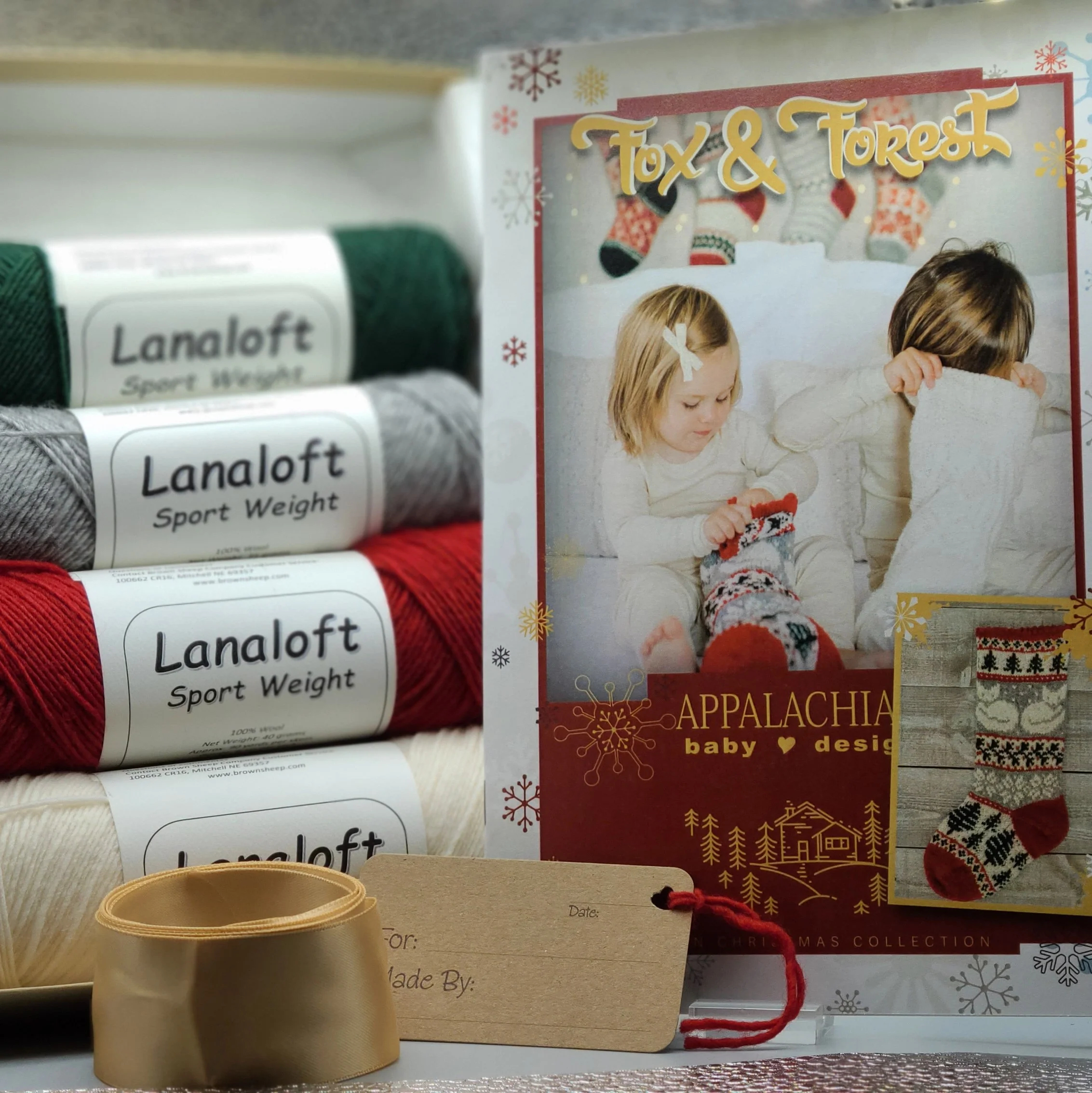 4 skeins of Lanaloft in holiday hues paired with a gift tag and Christmas stocking knitting kit