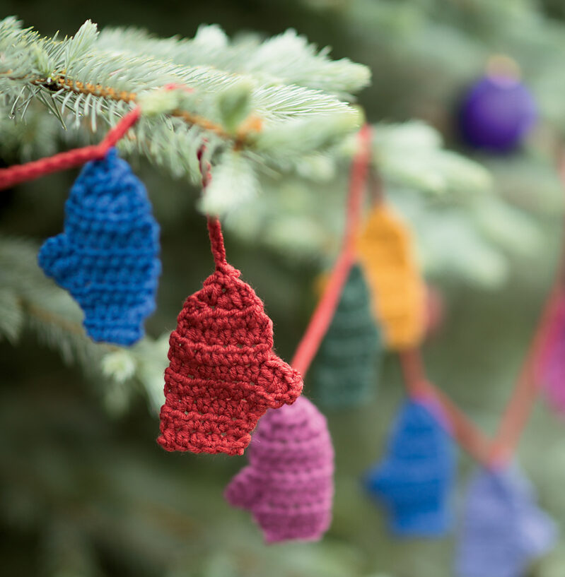 a garland of crocheted miniature mittens on an evergreen tree