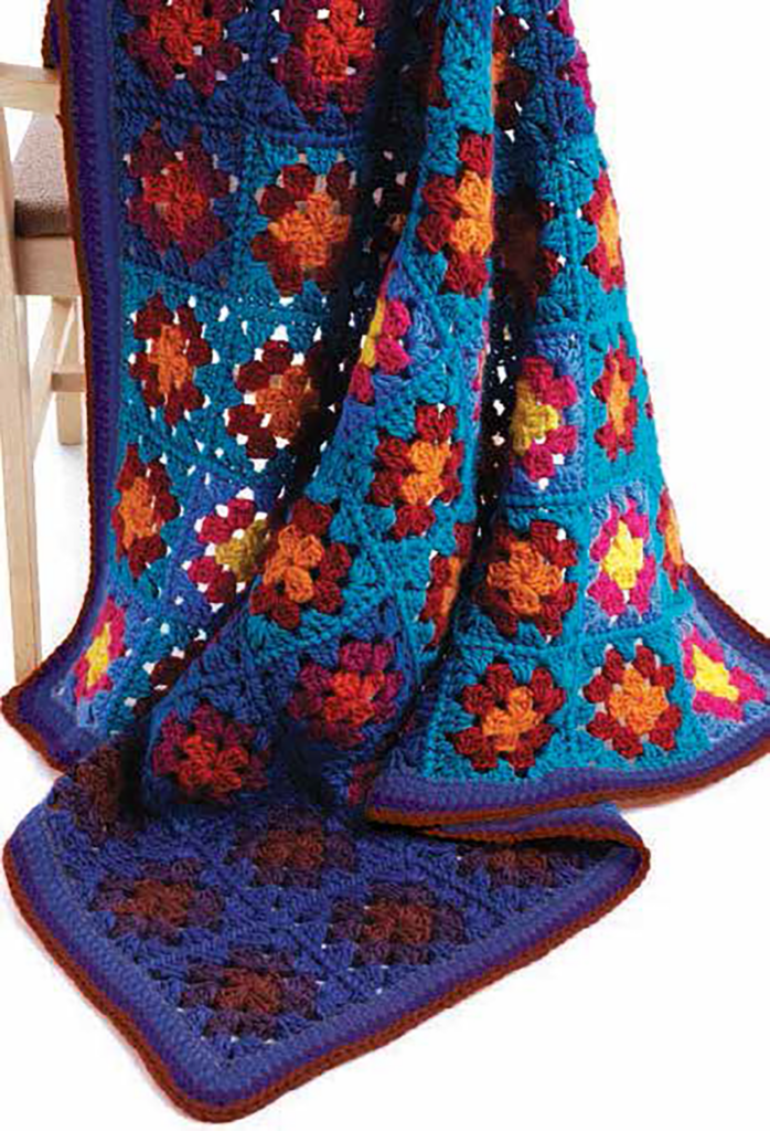 crochet granny square blanket in blue, purple, red and orange draped over a chair