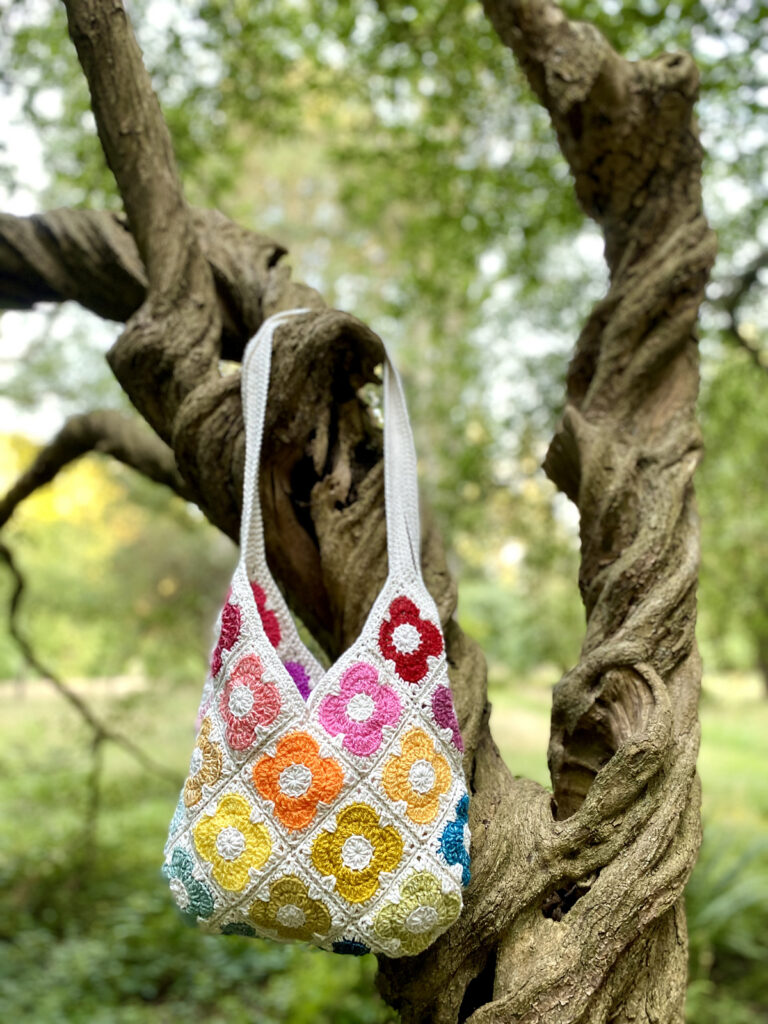 a multicolored granny square blag hanging from tree