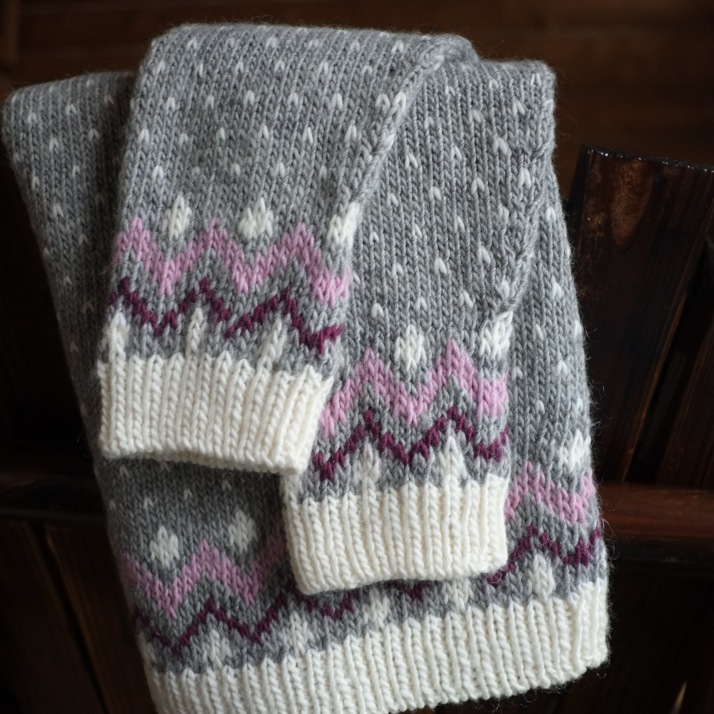 A colorwork sweater in great, cream, pink and maroon folded with the sleeves atop the body